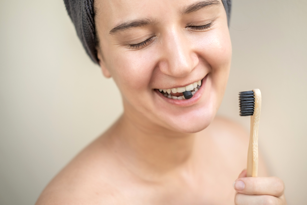 Vrouw poetst haar tanden met een tandpasta tablet en een bamboe tandenborstel, voor een duurzame mondverzorging