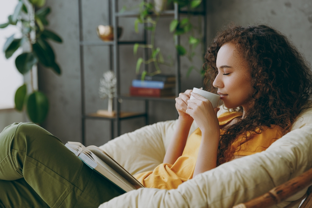 Vrouw ontspant met een kop thee en een boek in een gezellige, groene woonkamer